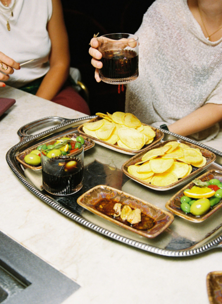 Bandeja de aperitivo con patatas chips, aceitunas y vaso de vermut sobre mesa de mármol