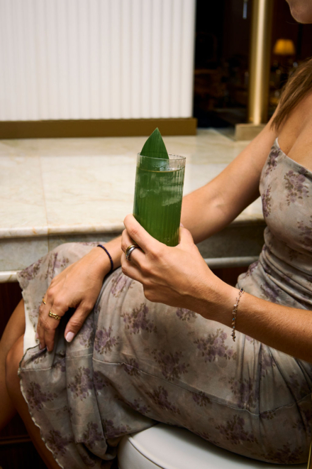 Mujer sentada con un cóctel verde decorado con hoja