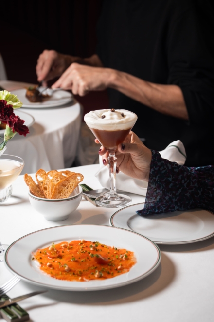 Espresso martini, patatas chips y plato para compartir sobre mesa con mantel blanco