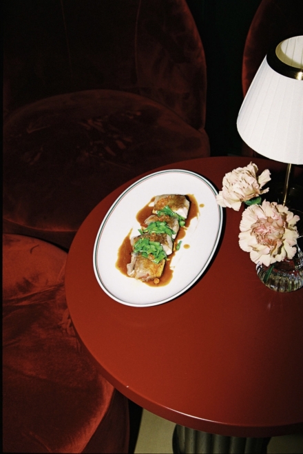 Plato de cocina de temporada con salsa y hierbas sobre mesa redonda roja con flores y lámpara